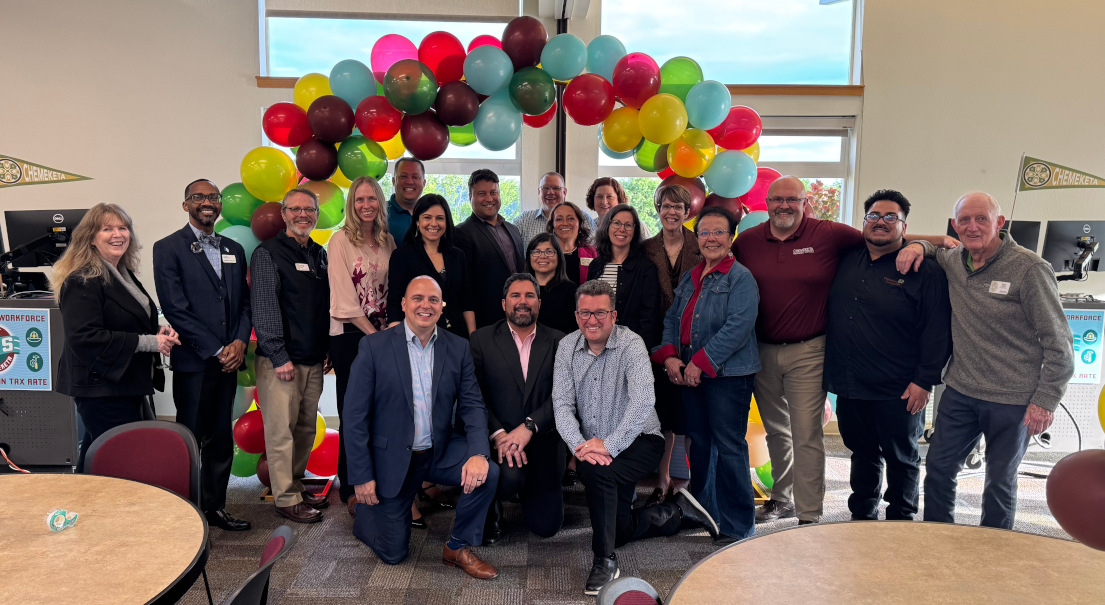 A group of Chemeketa employees and board members in a group photo. Behind them is a balloon arch with multi-colored balloons.